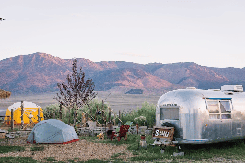 An rv with some tents next to it in the wilderness