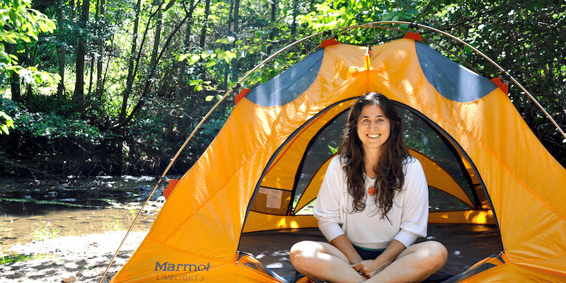 A woman sitting next to a tent and smiling 