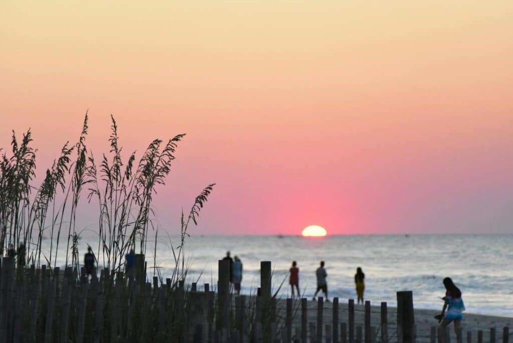 Serene beach sunset with silhouetted people and vibrant sky over the ocean.