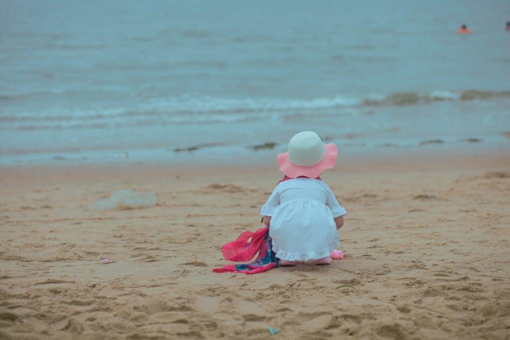 a little girl sitting in the sand at the beach