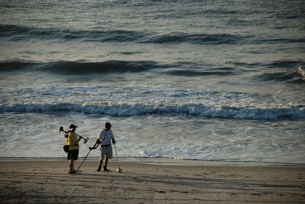 man in black shorts holding white and black stick standing on beach shore during daytime