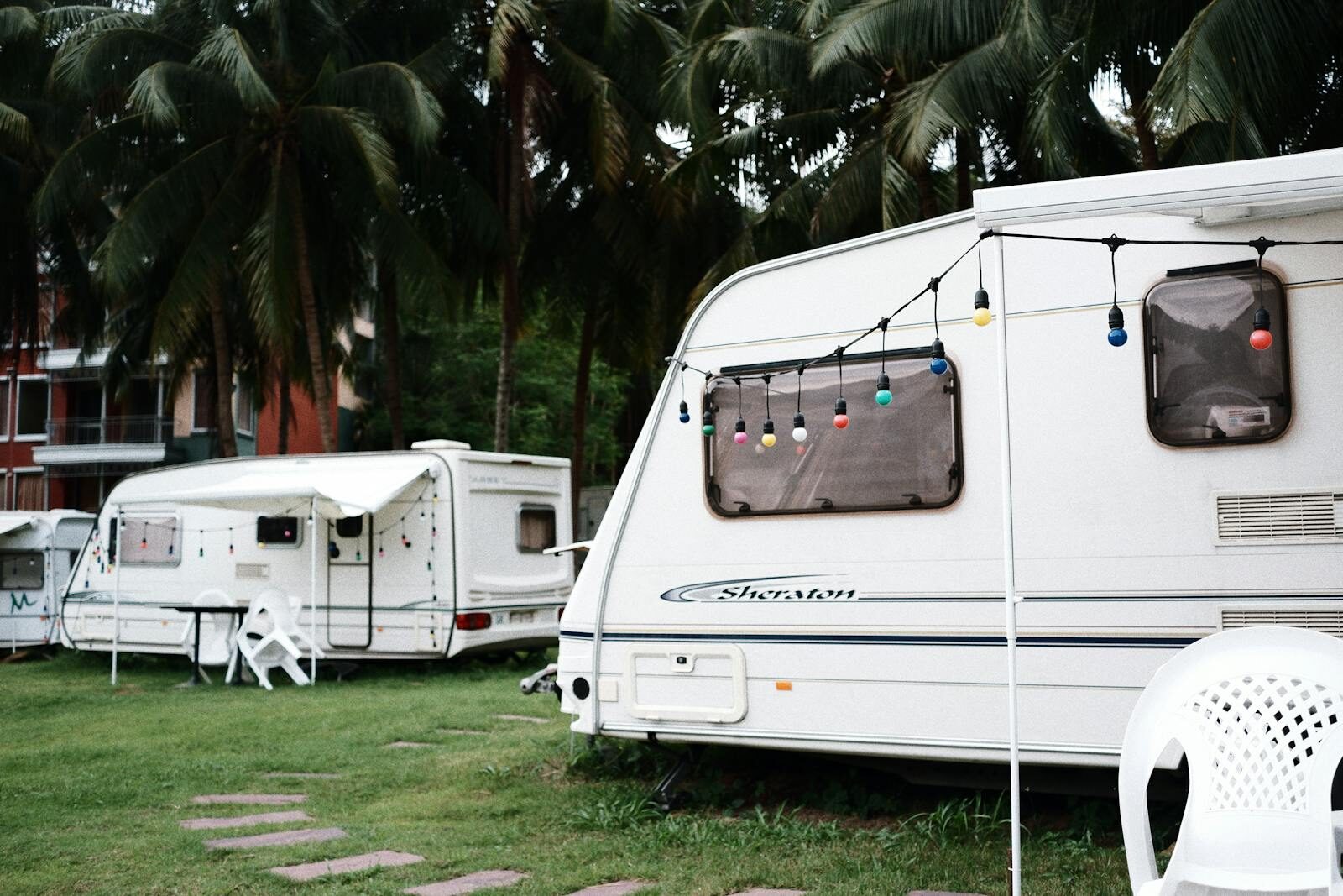 Photo by Mew wy. Relaxing caravan camping site under palm trees with outdoor seating and festive lights.
