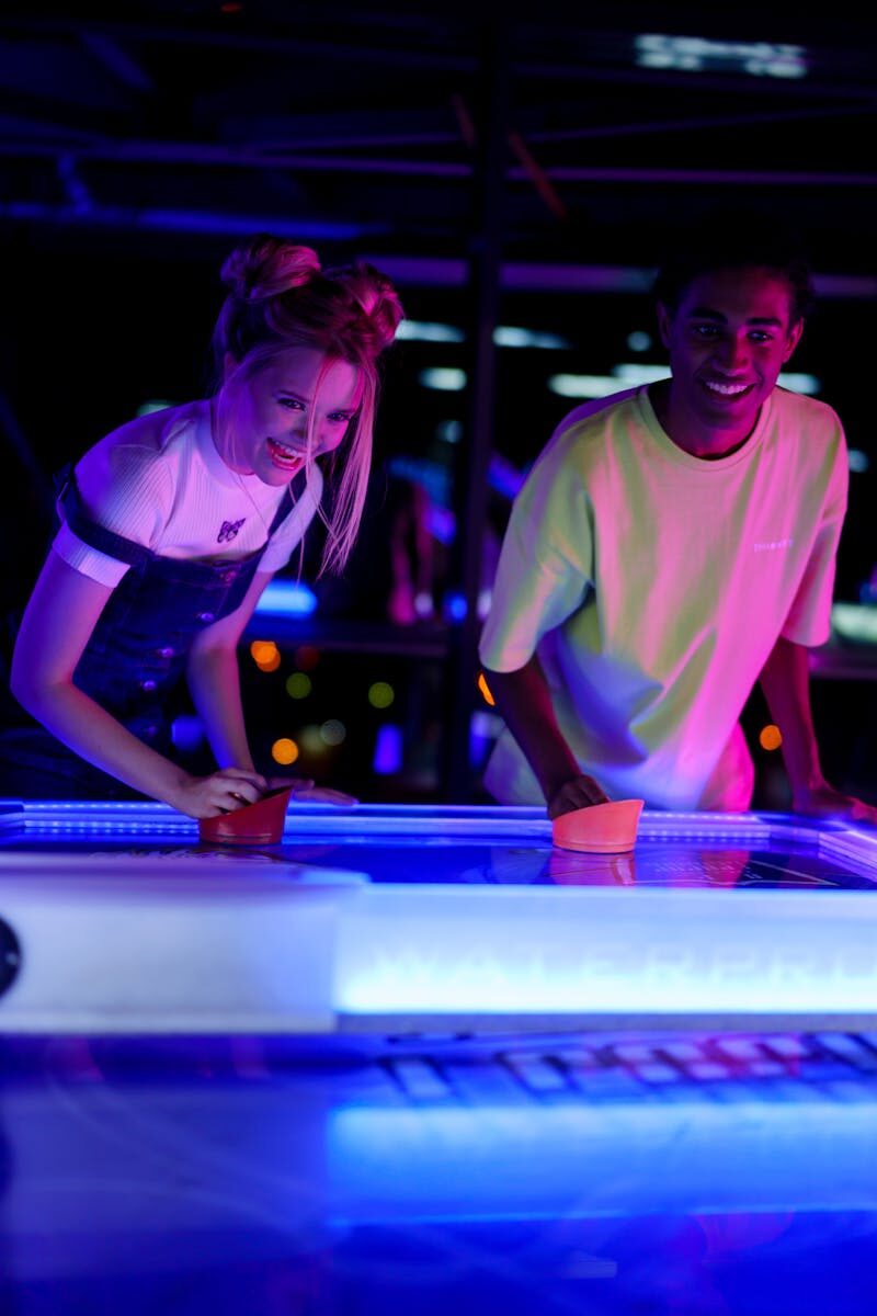 Photo by cottonbro studio Two young friends having fun playing air hockey in a neon-lit amusement arcade.