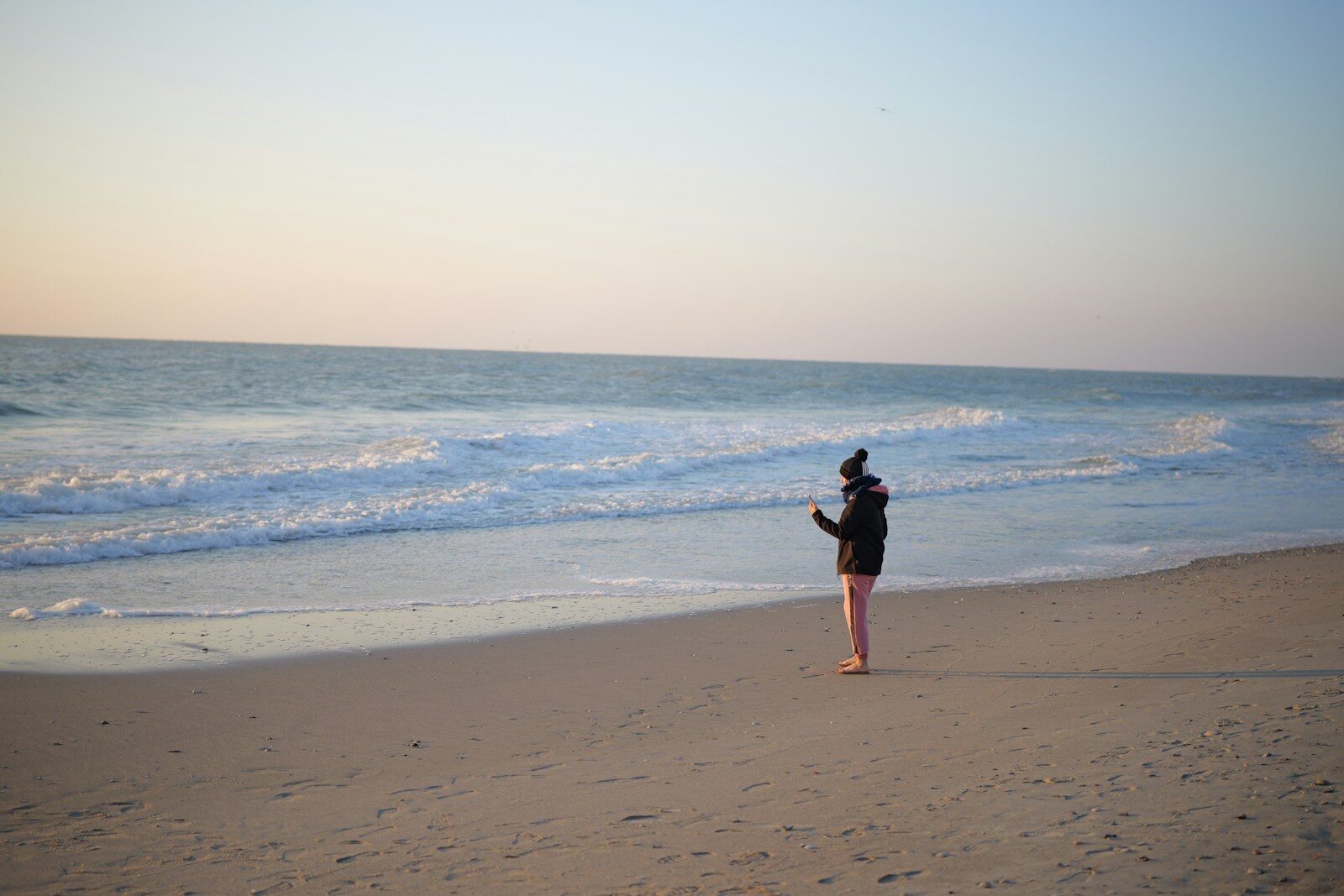 Photo by Yejiang Yang A person standing on a beach flying a kite