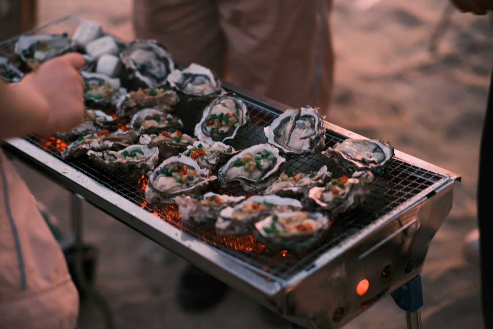 Photo by LI WEIBIN a person holding a tray of oysters on a grill